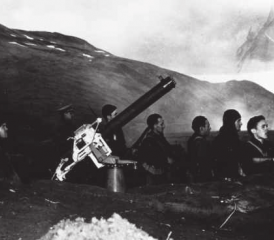 3. Juni 1942, Durch Harbor, Aleuten. Die Crew einer Maschinengewehrstellung beobachtet die abfliegenden japanischen Kampfflugzeuge. Im Hintergrund der Rauch der von japanischen Sturzkampfbombern in Brand geschossenen SS Nortwestern.